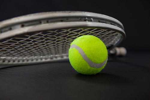 Close up of ball and silver tennis racket against black background