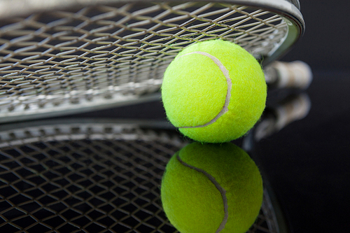 Close up of tennis racket on ball with reflection against black background