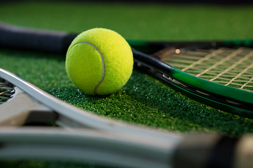 Close up of tennis ball with rackets on field