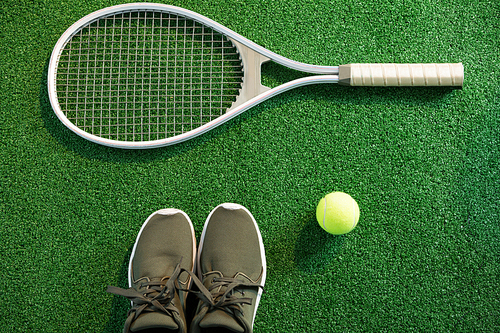 Close up of racket with shoes and tennis ball on playing field