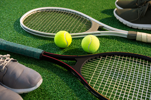 Close up of tennis rackets with balls and sports shoes on field