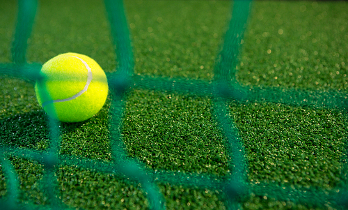 Close up of tennis ball seen through net on court