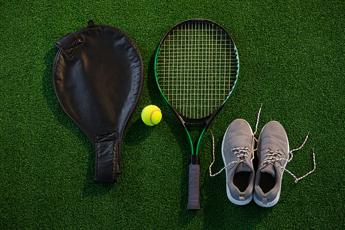 Directly above shot of racket with ball and sports shoes on field