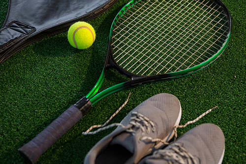 Close up of racket with ball and sports shoes on court