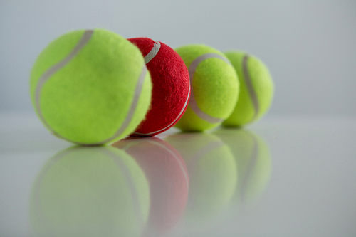 Red and fluorescent tennis ball arranged in row against white background