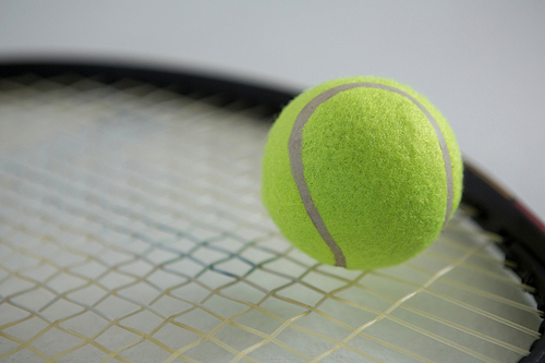 Close up of fluorescent tennis ball on racket against white background