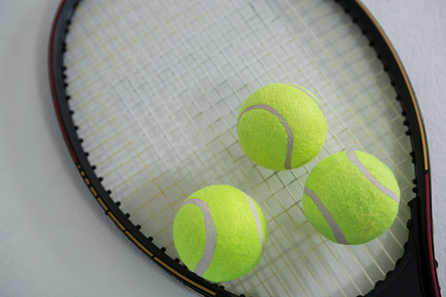 Close up of fluorescent yellow tennis ball on racket against white background