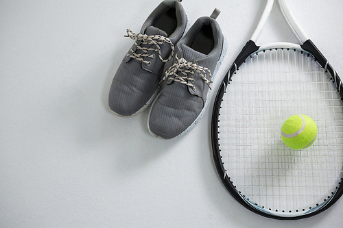 Close up of racket with tennis ball by sports shoe on white background