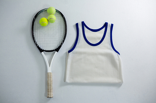 Overhead view of racket with tennis balls by vest on white background