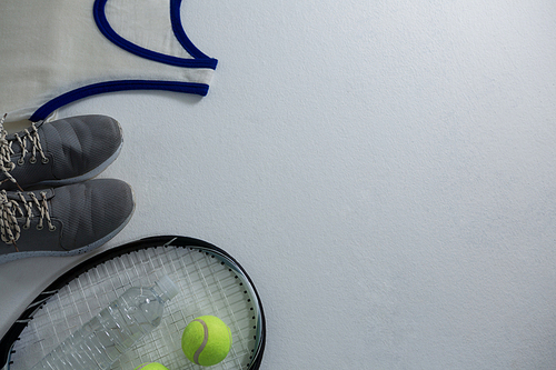 Cropped image of racket with ball and sports shoe by vest on white background