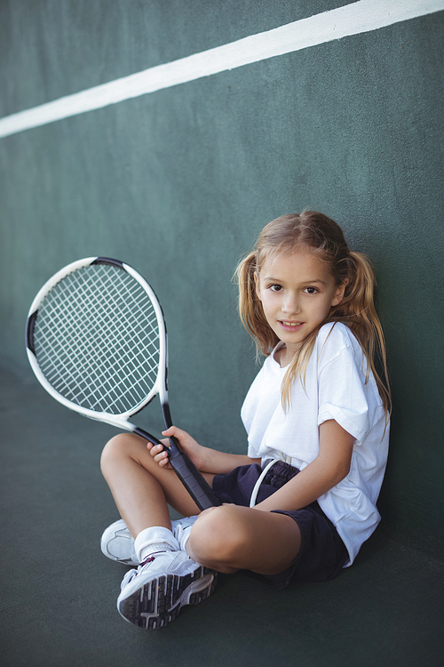 Full length portrait of girl holding tennis racket while sitting at court