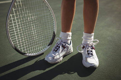 Low section of girl with tennis racket standing on court