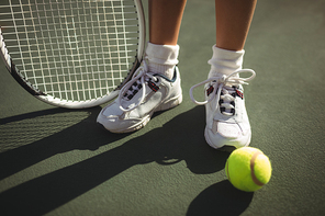 Low section of girl with racket standing by tennis ball on court