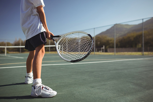 Low section of girl holding tennis racket while standing on court