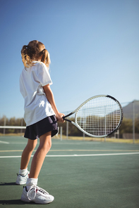 Side view of girl holding tennis racket while standing on court