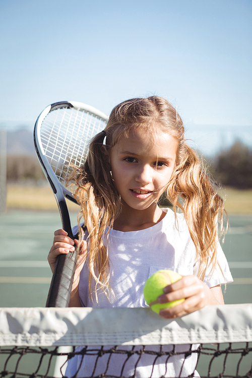 Portrait of girl holding racket and tennis ball at court on sunny day