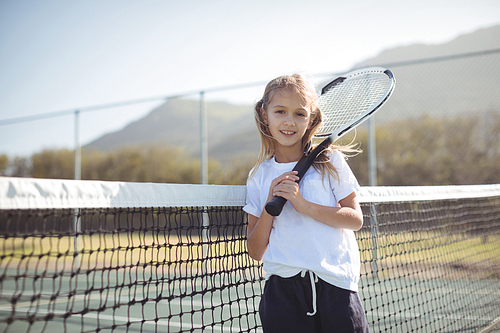 Portrait of smiling girl holding tennis racket while standing by net at court