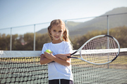 Portrait of confident girl holding tennis racket and ball at court during sunny day