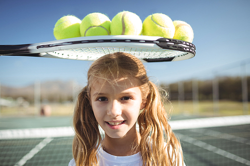 Portrait of smiling girl standing below tennis racket and balls at court