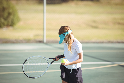 Girl holding tennis ball and racket while standing on court during sunny day
