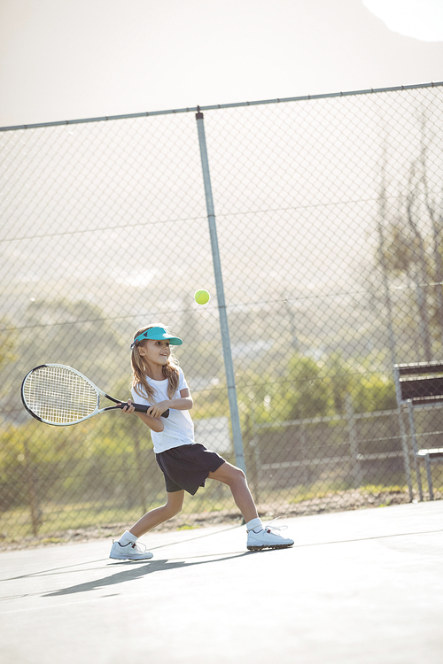 Girl playing tennis against fence on court during sunny day
