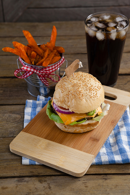 Hamburger, french fries and cold drink on table against wooden background