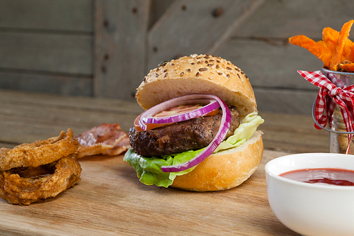 Close-up of hamburger, french fries, onion ring and tomato sauce on chopping board