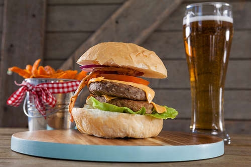 Hamburger, french fries and glass of beer on table against wooden background