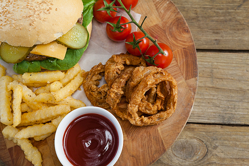 Overhead of hamburger, onion ring, tomato sauce, cherry tomato and french fries on chopping board