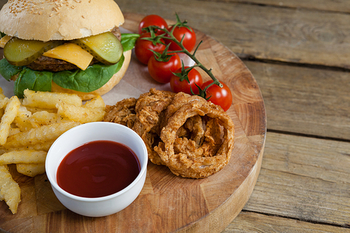 Close-up of hamburger, onion ring, tomato sauce, cherry tomato and french fries on chopping board