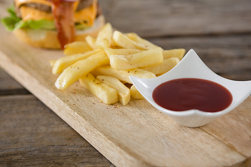 Close up of tomato sauce in bowl by french fries on cutting board