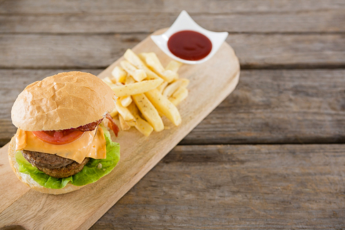 High angle view of french fries with burger and sauce on cutting board at table