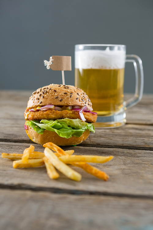 Close up fries with burger and beer glass on table against wall