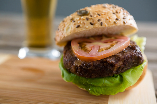 Close up of hamburger on cutting board with beer glass in background