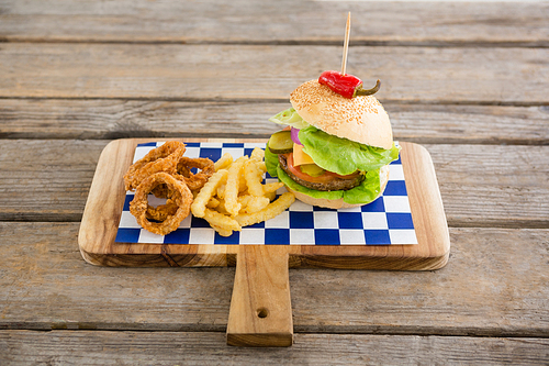 Hamburger with onion rings and french fries on cutting board at table