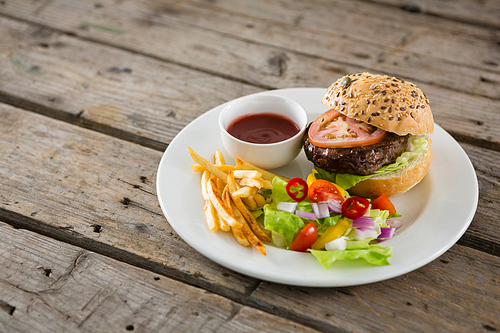 Close up of salad with burger and french fries in plate on table