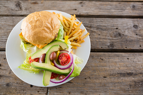 Overhead view of cheeseburger with salad and french fries served in plate on table