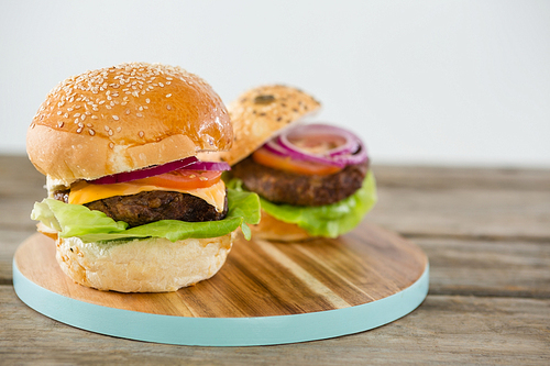 Burgers on cutting board at table against white background