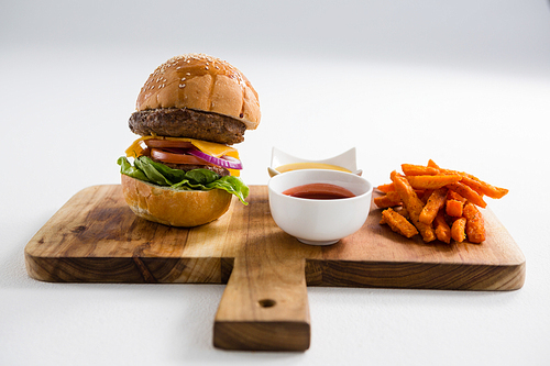 Dips with French fries and burger on cutting board at table against white background