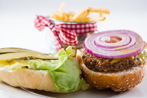 Close up of open burger by French fries in container on plate against white background