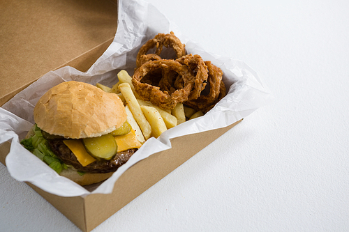 Close up of burger with onion rings and French fries in box on table