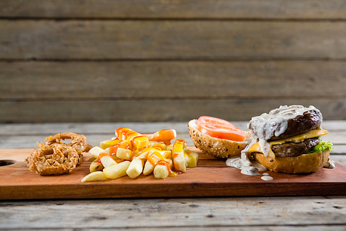 Close up of French fries with sauce and burger and onion rings on cutting board