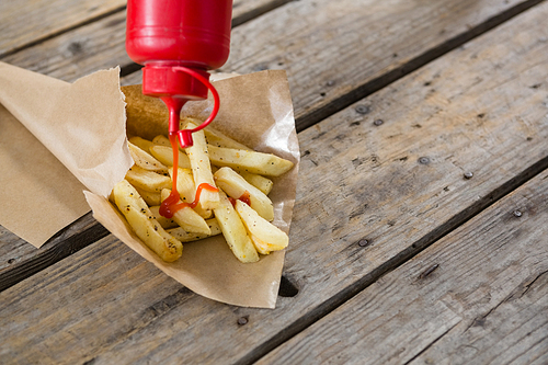 High angle view of bottle pouring sauce on French fries in paper on wooden table