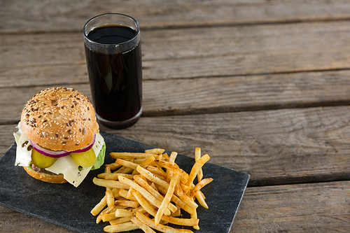 High angle view of cheeseburger with french fries and drink on slate at wooden table