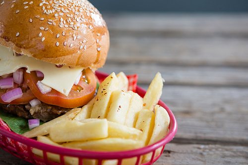 Close up of French fries and cheeseburger in basket on wooden table