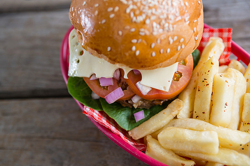 High angle view of cheeseburger with French fries in basket on wooden table