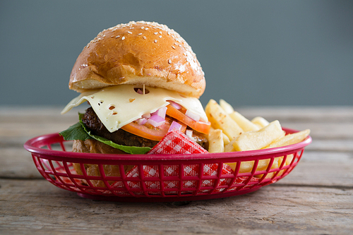 Close up of cheeseburger and French fries in basket on wooden table against wall