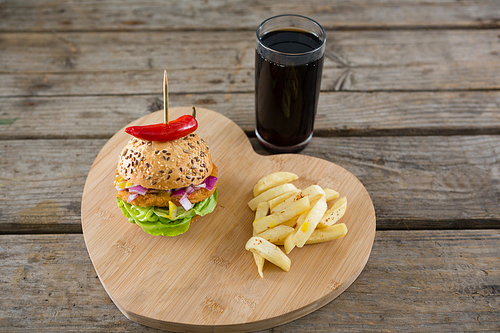 High angel view of burger with French fries on heart shape cutting board by drink at wooden table