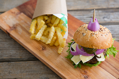 High angle view of burger by French fries in box on cutting board at table against wall