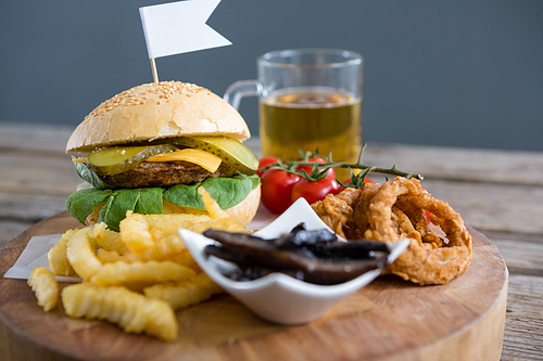 Vegetables with fried food by burger and beer on table against wall